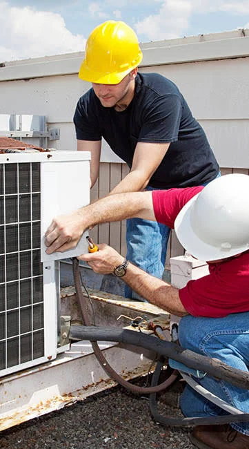 Two HVAC technicians working together on an outdoor air conditioning unit